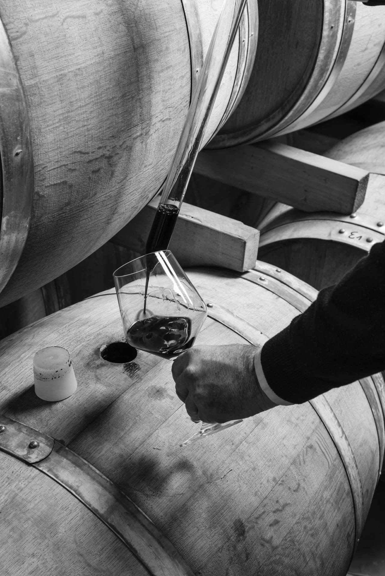 Italy, Sicily, red wine pouring from a wooden barrel into a glass in a wine cellar